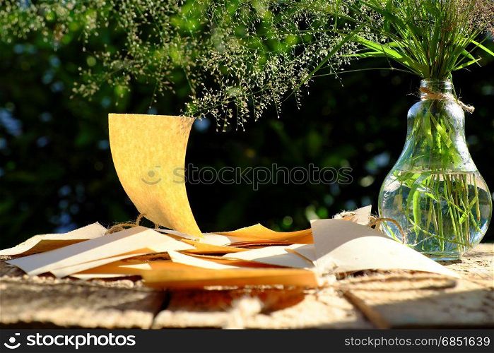 Flower grass in glass jar with note paper in wind blow at evening sun make feeling and calm, wild tiny flowers on green natural background in garden