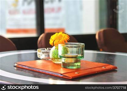 Flower, menu and candle on table in cafe.