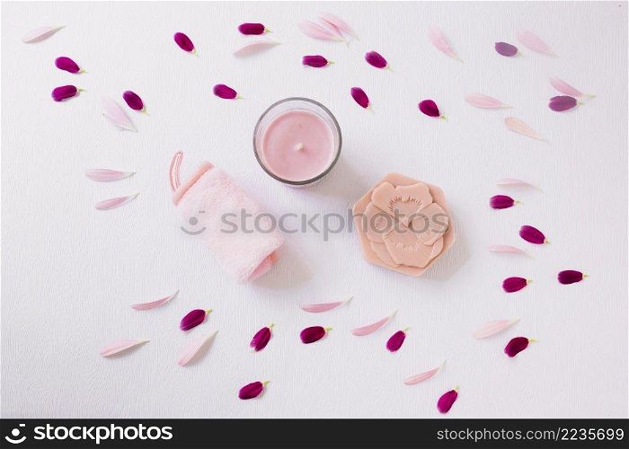 flower petals around rolled up soft napkin candle soap white background