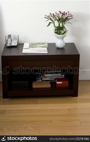 Flower vase with books and a cordless phone on a side table