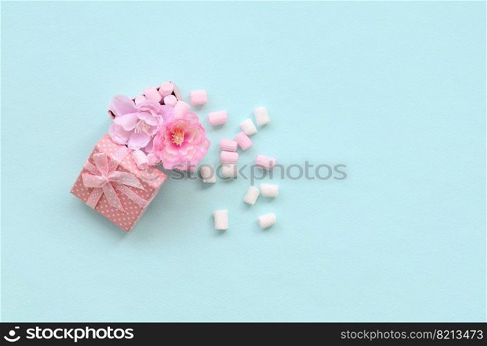 Flowered pink gift box sprinkled with marshmallows on blue background. Metaphorical concept processing and cultivation of flowers. Minimalism flat lay. Top view. Flowered pink gift box sprinkled with marshmallows on blue background