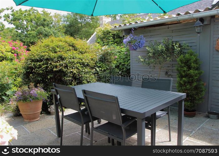 Flowered terrace with flowerpots, gray garden furniture and green sunshade during spring