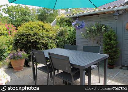 Flowered terrace with flowerpots, gray garden furniture and green sunshade during spring