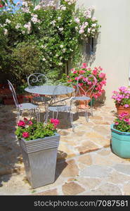 Flowered terrace with gray garden furniture and some flowerpots with geraniums in spring