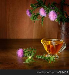 Flowering plant milk thistle and oil glass. Healing herb on wooden background. Free space for text.