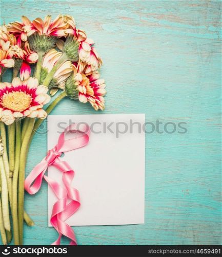 Flowers bunch with blank white greeting card and pink ribbon on shabby chic blue turquoise background, top view.