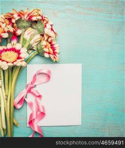 Flowers bunch with blank white greeting card and pink ribbon on shabby chic blue turquoise background, top view.