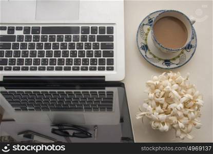 Flowers, coffee and laptop on a white wooden table that looks relaxed