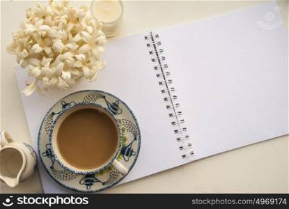 Flowers, coffee and notebooks on a white wooden table that looks relaxed