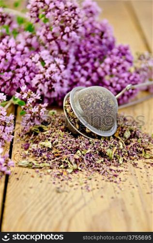 Flowers fresh and dry oregano in a metal strainer on a wooden boards background