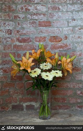 flowers in a vase standing in the background of a brick wall
