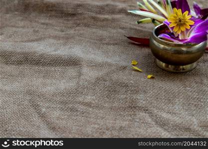 Flowers in brass cups in corner on burlap fabric background, in the upper right corner of the background ready for your text or message, copy space.