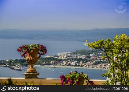 Flowers in pot with a background of the sicilian coast at the height of the city of taormina italy