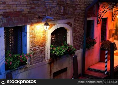 Flowers on the windows of an old house in Venice at night, Italy. Facade of venetian house
