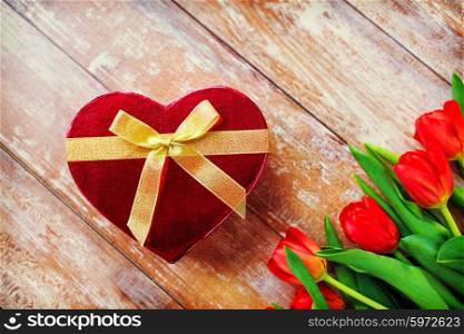 flowers, valentines day and holidays concept - close up of red tulips and heart shaped chocolate box on wooden table