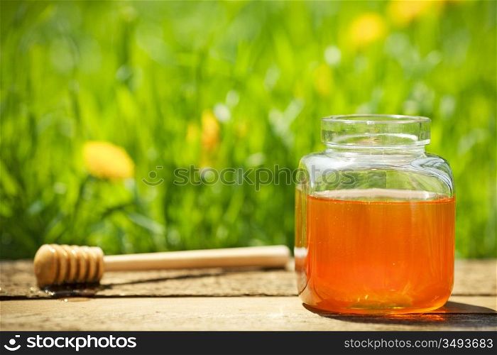 Flowery honey in glass jar on wooden table against spring natural green background