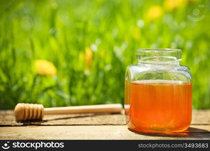 Flowery honey in glass jar on wooden table against spring natural green background