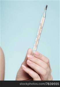 Flu cold fever symptom. Closeup of medical mercury thermometer in female hand on blue. Health care.