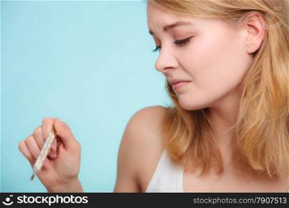 Flu cold grippe symptom. Woman having high temperature. Sick girl with fever checking mercury thermometer on blue.
