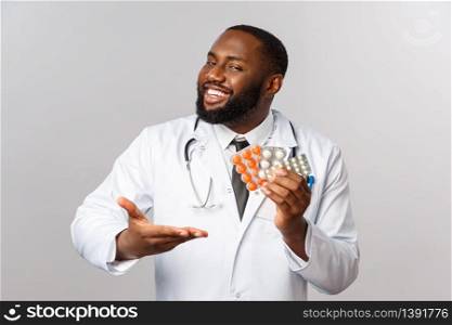 Flu, disease, healthcare and medicine concept. Happy african-american male doctor in white coat present new drugs, cure from disease or viruses, showing pills guarantee good quality of treatment.. Flu, disease, healthcare and medicine concept. Happy african-american male doctor in white coat present new drugs, cure from disease or viruses, showing pills guarantee good quality of treatment