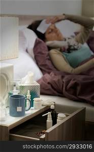Flu medicines on bedside table beside ill woman in bed