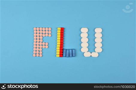 Flu season or influenza concept. The word flu made from the assorted pills and capsules on blue background. Pharmacy theme, health care, drug prescription for medication treatment. Flu season or influenza concept. The word flu made from the assorted pills and capsules on blue background.