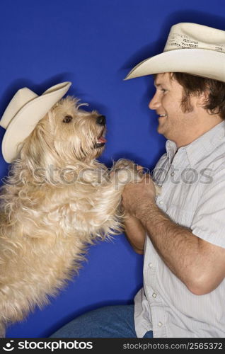 Fluffy brown dog and male Caucasian young adult wearing cowboy hats.