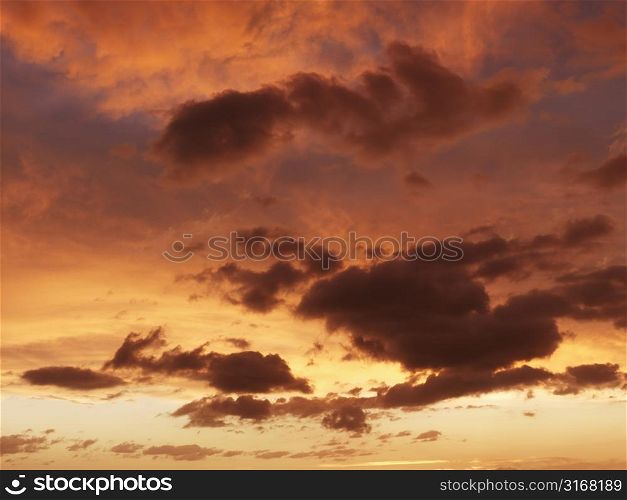 Fluffy clouds in orange-colored sky at sunset.