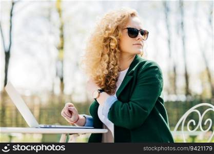 Fluffy-haired woman translating, noticing best friend enjoying sunny yard. Pretty, sunglasses, laptop.