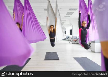 Fly yoga, female group training, hanging on hammocks. Fitness, pilates and dance exercises mix. Women on yogi workout in sports studio. Fly yoga, female group hanging on hammocks