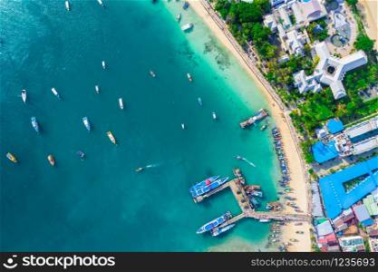 Flying above busy tropical island port filled with boats and ferries. Countless ships sail to and from bustling harbor on exotic beach. Picturesque shot of fleet of anchored longtail boats.