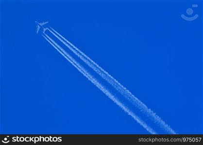 Flying aeroplane with leaving white trails on a blue sky