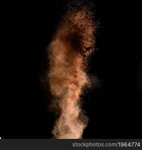 flying brown cocoa particles on a black background. Powder flies up