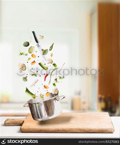 Flying cooking ingredients for vegetables stock, broth or soup with pot and knife on table at kitchen background. Healthy vegetarian food concept
