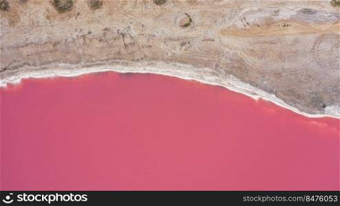Flying over a pink salt lake. Salt production facilities saline evaporation pond fields in the salty lake. Dunaliella salina impart a red, pink water in mineral lake with dry cristallized salty coast. Flying over a pink salt lake. Salt production facilities saline evaporation pond fields in the salty lake. Dunaliella salina impart a red, pink water in mineral lake with dry cristallized salty coast.