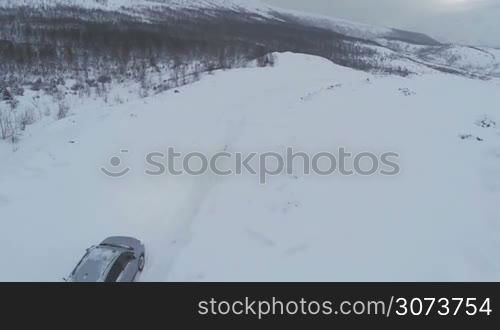 Flying over offroader car driving on heavy snowy road. Winter landscape with mountains and bare trees