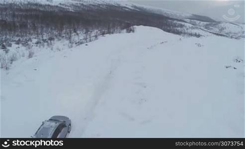 Flying over offroader car driving on heavy snowy road. Winter landscape with mountains and bare trees