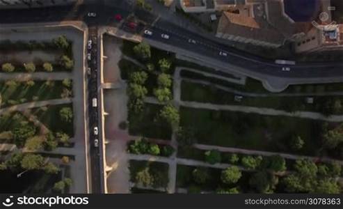 Flying over the green park with paths, houses with rooftops and cars on the roads in Valencia, Spain