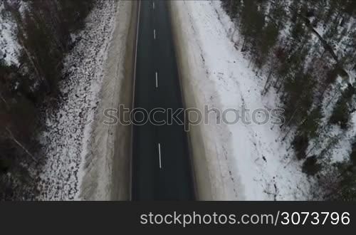 Flying over the road with no cars in winter. Snowy northern land and rare trees alongside the way