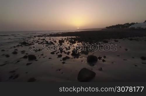 Flying over the rocks on the coast and ocean waves at sunset. Gran Canaria, Canary Islands