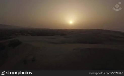 Flying over vast sand landscape with dunes and plants at sunset, Gran Canaria