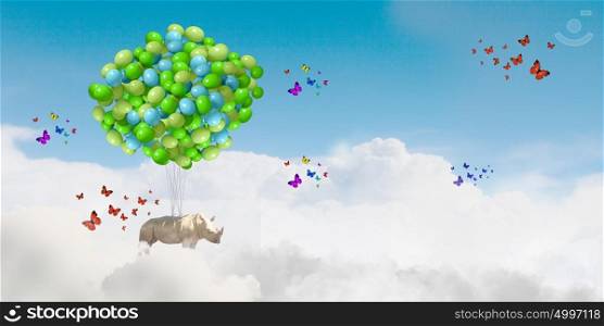 Flying rhino. Rhino flying high in sky on bunch of colorful balloons