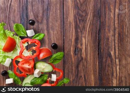flying salad on wooden background - red tomatoes, pepper, cheese, basil, cucumber and olives