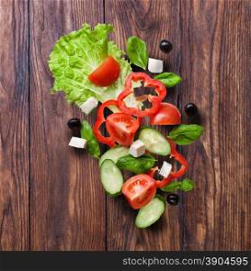 flying salad on wooden background - red tomatoes, pepper, cheese, basil, cucumber and olives