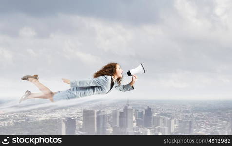 Flying superwoman. Young pretty businesswoman flying in blue sky sreaming in megaphone