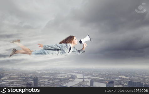 Flying superwoman. Young pretty businesswoman flying in blue sky sreaming in megaphone