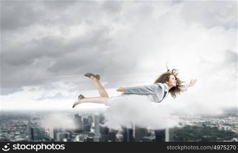 Flying superwoman. Young pretty businesswoman flying in sky above city