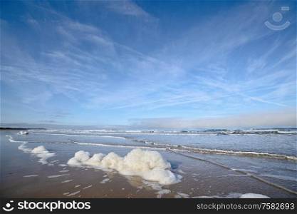 Foam on the beach by the ocean under a blue sky with waves coming in