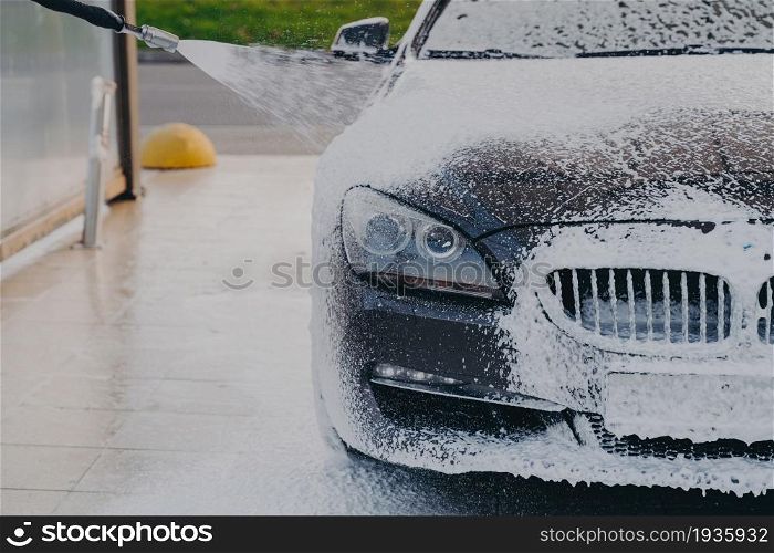 Foaming exterior of vehicle with foam gun. Outdoor vehicle washing. Cleaning process of dirty car with high pressure washer at self-service station, luxury auto in white soap snow foam. Car in white soap snow foam at carwashing center outdoors