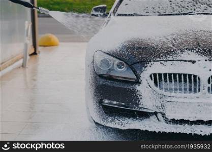 Foaming exterior of vehicle with foam gun. Outdoor vehicle washing. Cleaning process of dirty car with high pressure washer at self-service station, luxury auto in white soap snow foam. Car in white soap snow foam at carwashing center outdoors
